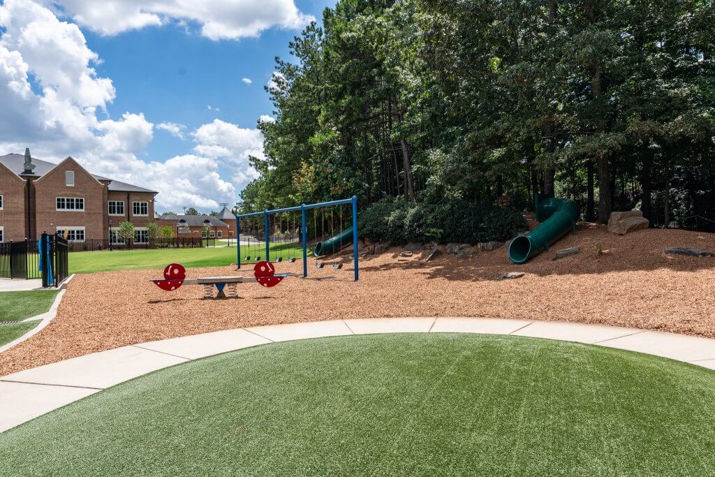 A vibrant outdoor children's playground features various climbing structures and slides, all set upon a thick layer of natural dark wood mulch ground cover. The mulch provides a safe, cushioned surface throughout the entire play area.