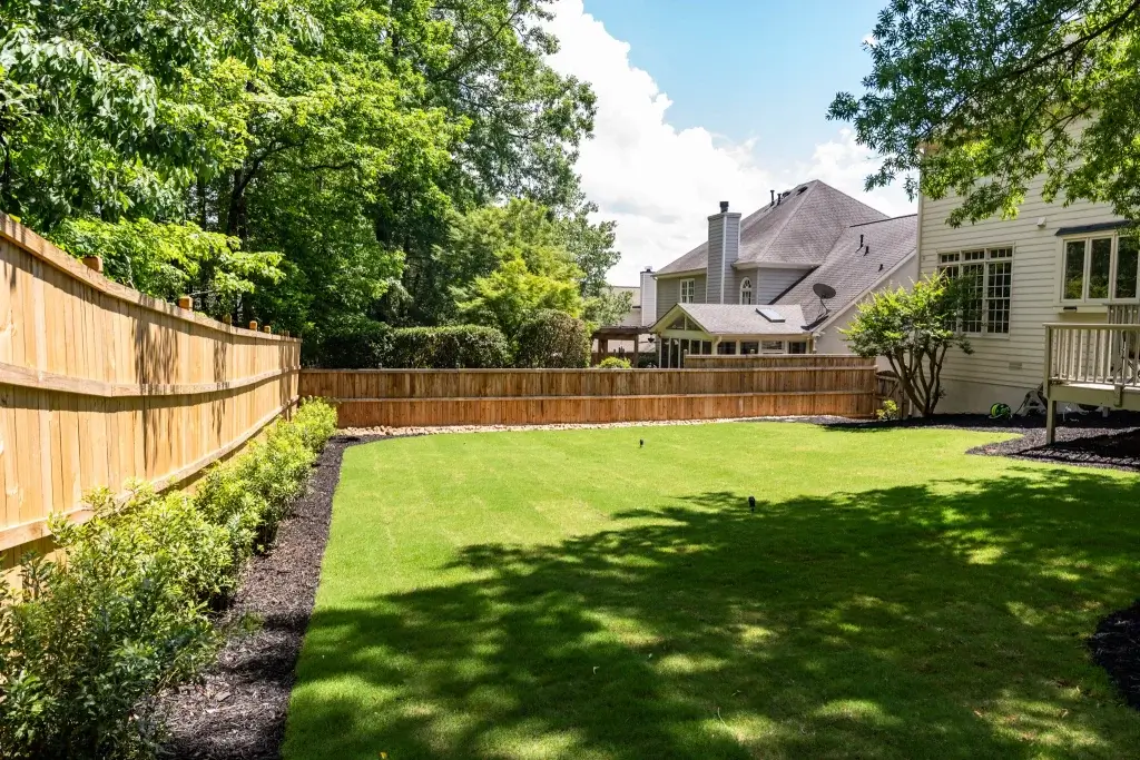 Professional grounds crew performing fall landscaping services Atlanta by clearing leaves, installing fresh pine straw, and aerating a large commercial lawn.